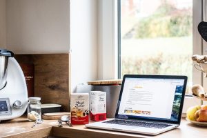 Laptop stojący na kuchennym blacie przy oknie obok produktów spożywczych